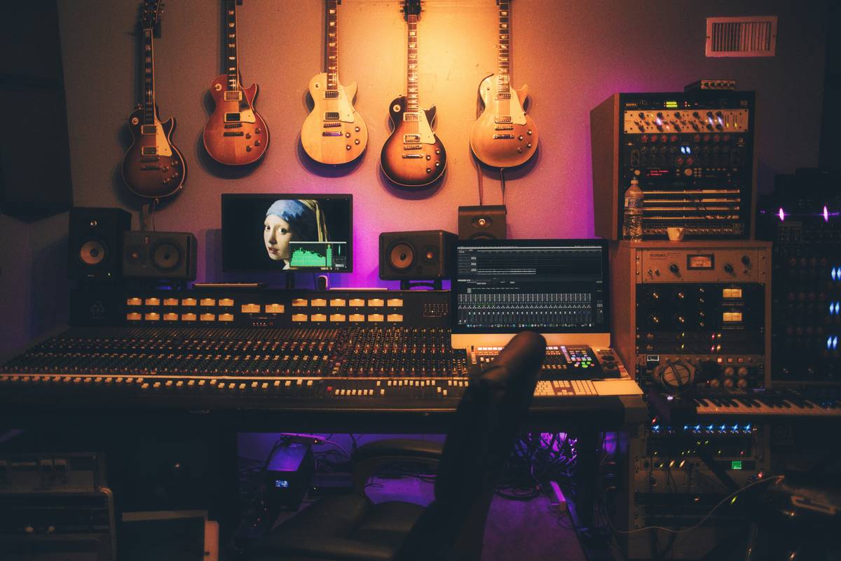 A professionally lit home studio setup with headphones, condenser mic, acoustic panels, and laptop screen showing podcast editing software — network marketing resources podcast